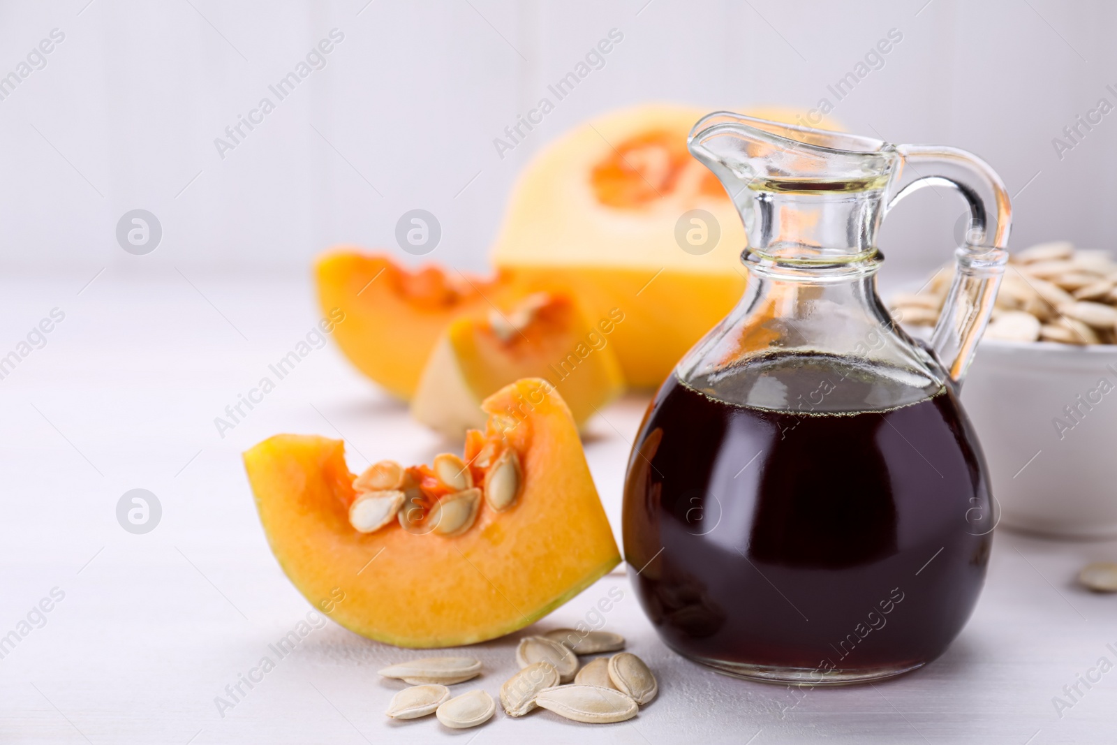 Photo of Fresh pumpkin seed oil in glass jug on white wooden table. Space for text