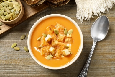 Photo of Tasty creamy pumpkin soup with croutons and seeds in bowl on wooden table, flat lay