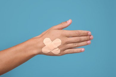 Photo of Man with sticking plasters on his hand against light blue background, closeup