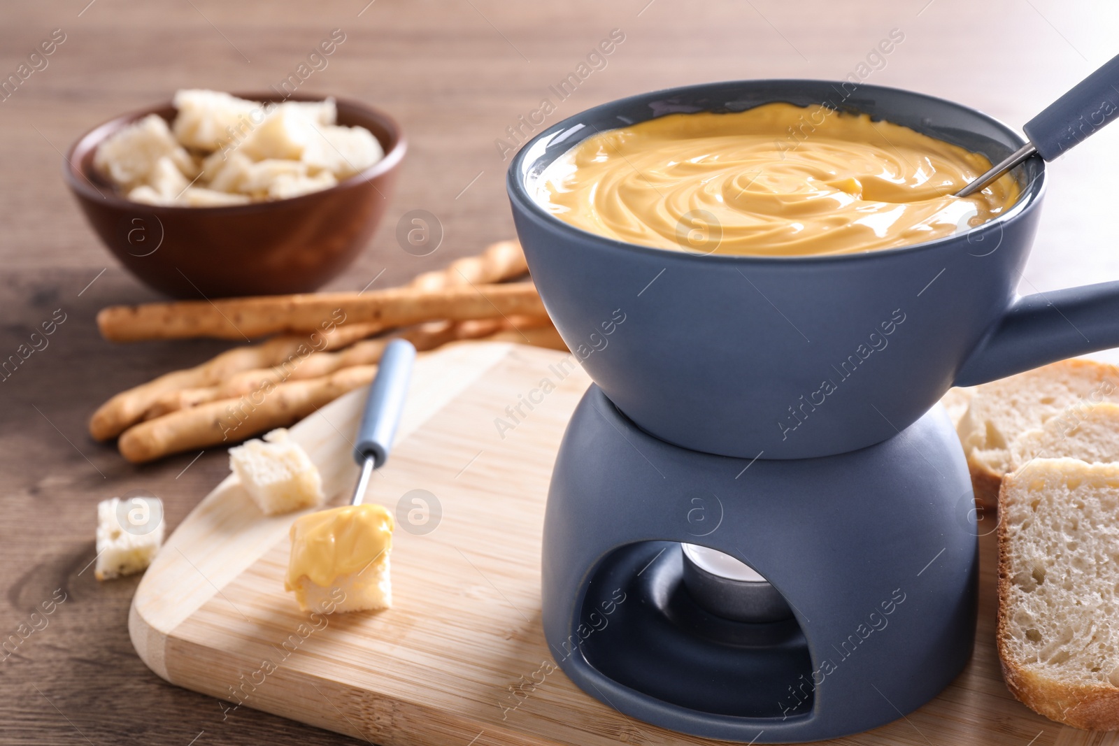 Photo of Board with pot of cheese fondue, bread and fork on table, space for text