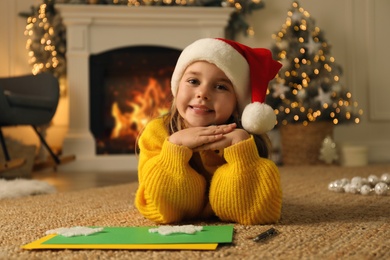 Cute child in Santa hat lying on floor at home. Christmas celebration