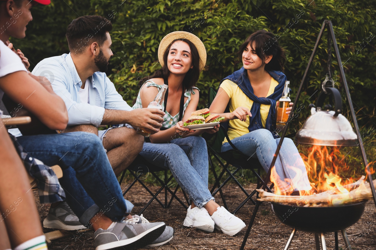 Image of Happy friends sitting near bonfire. Camping season