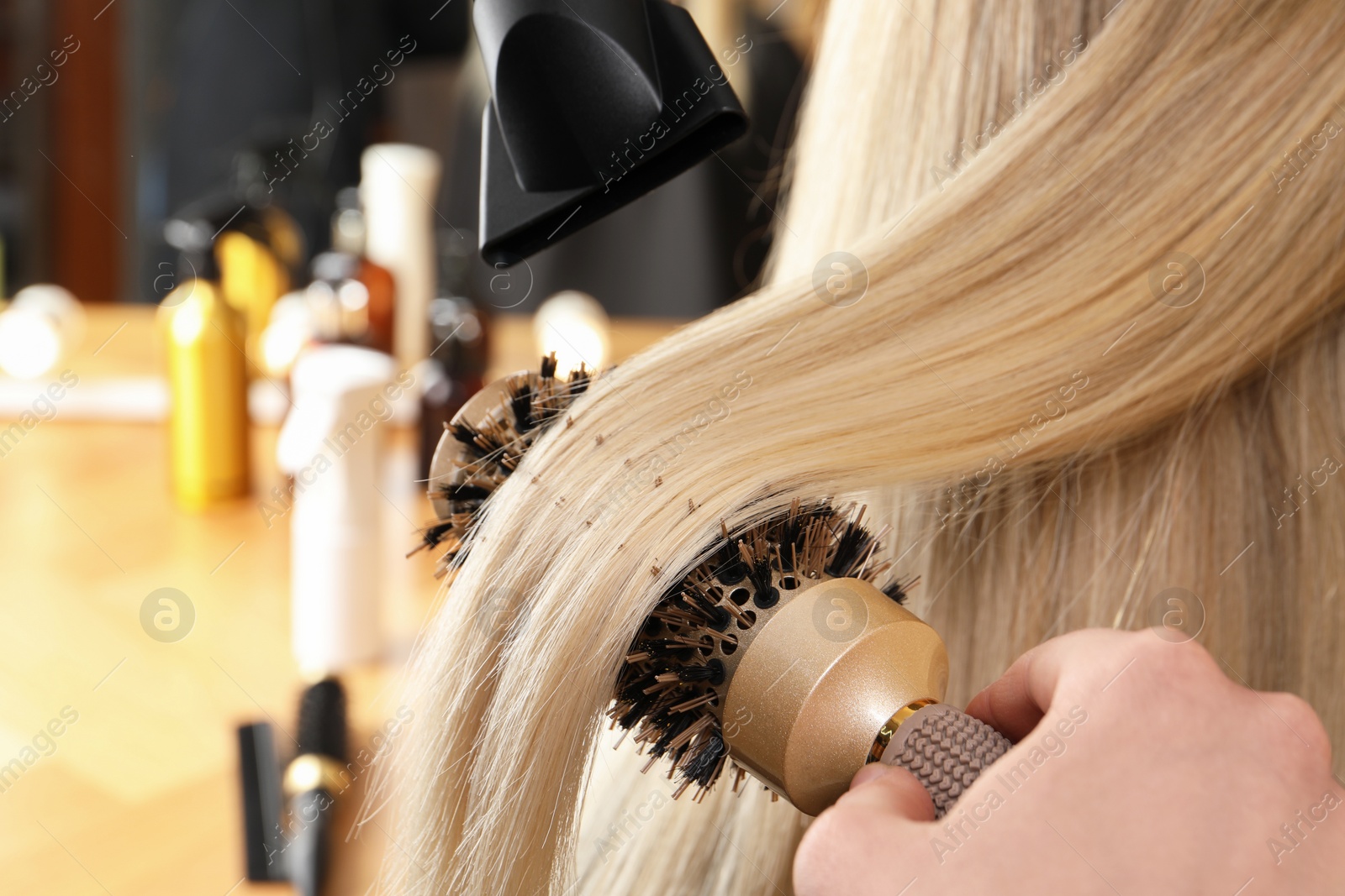 Photo of Hairdresser blow drying client's hair in salon, closeup