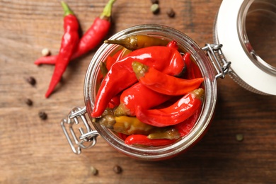 Glass jar with pickled peppers on wooden table, flat lay