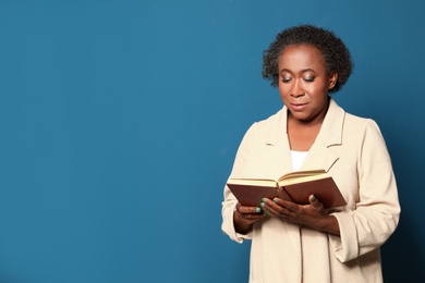 Portrait of mature African-American woman reading book on blue background, space for text