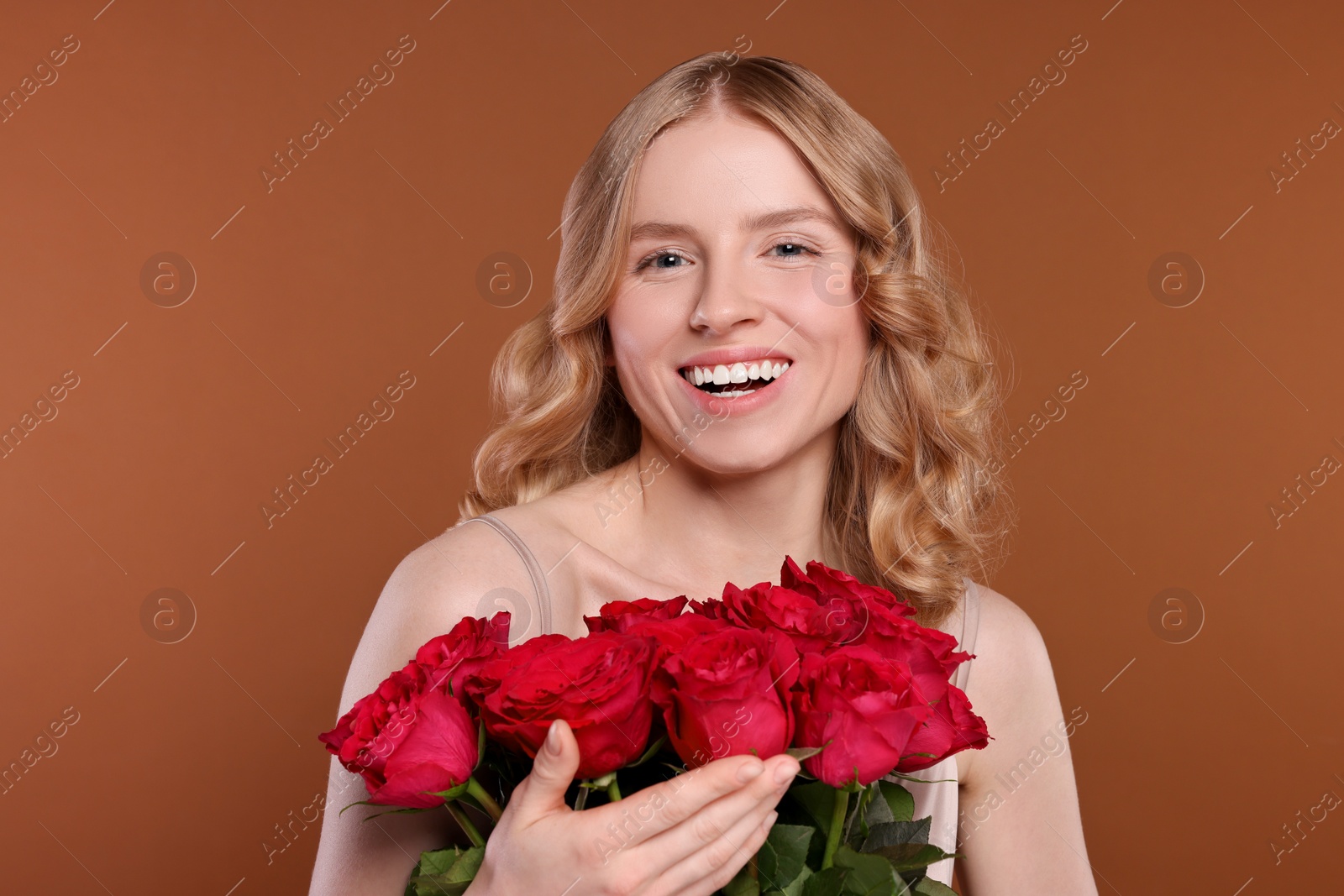 Photo of Beautiful woman with blonde hair holding bouquet of red roses on brown background