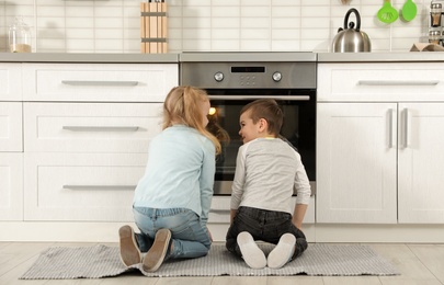 Photo of Little kids waiting for preparation of buns in oven at home