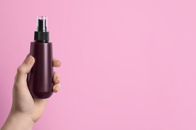 Photo of Woman holding spray bottle with thermal protection on light pink background, closeup. Space for text