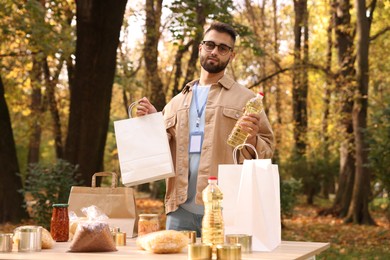 Portrait of volunteer with paper bag and food products on table in park
