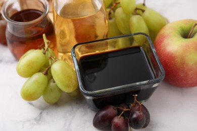 Photo of Different types of vinegar and ingredients on light marble table, closeup