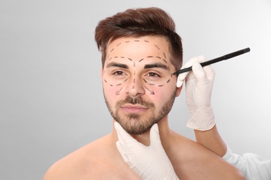 Photo of Doctor drawing marks on man's face for cosmetic surgery operation against grey background