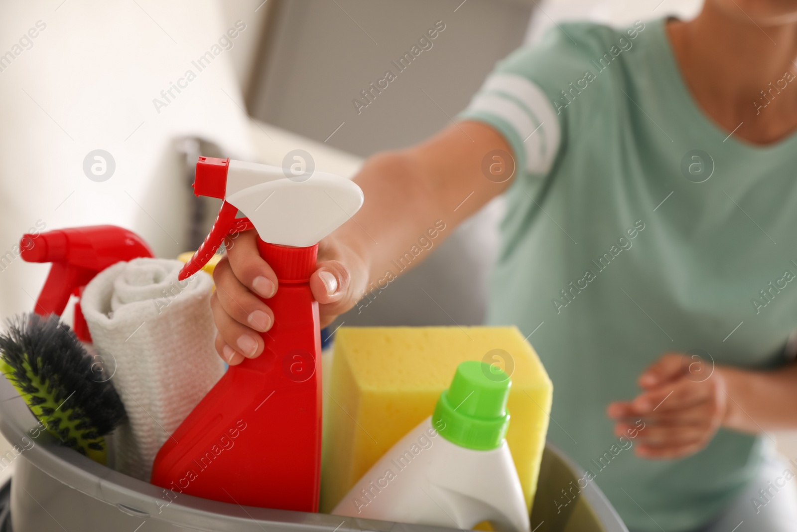 Photo of Woman taking bottle of detergent from bucket with cleaning supplies indoors, closeup