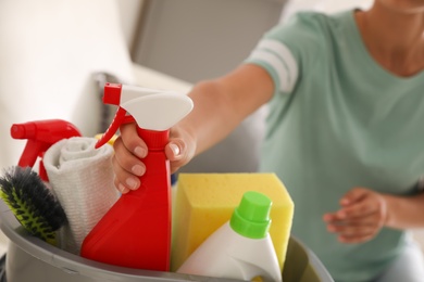 Woman taking bottle of detergent from bucket with cleaning supplies indoors, closeup