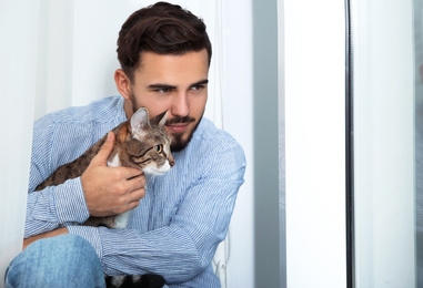 Photo of Man with tabby cat near window at home. Friendly pet