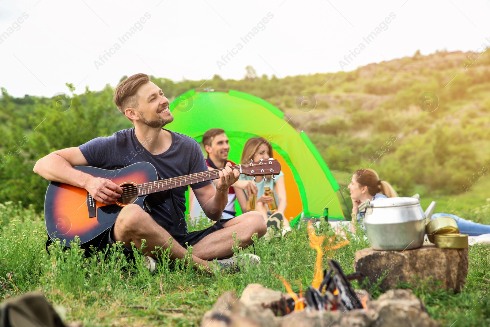 Photo of Man playing guitar near camping tent in wilderness
