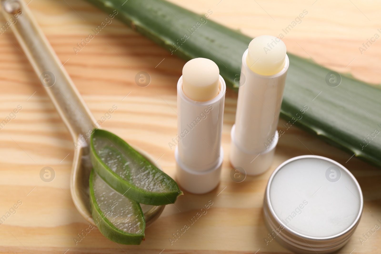 Photo of Different lip balms and aloe vera plant on wooden table, closeup