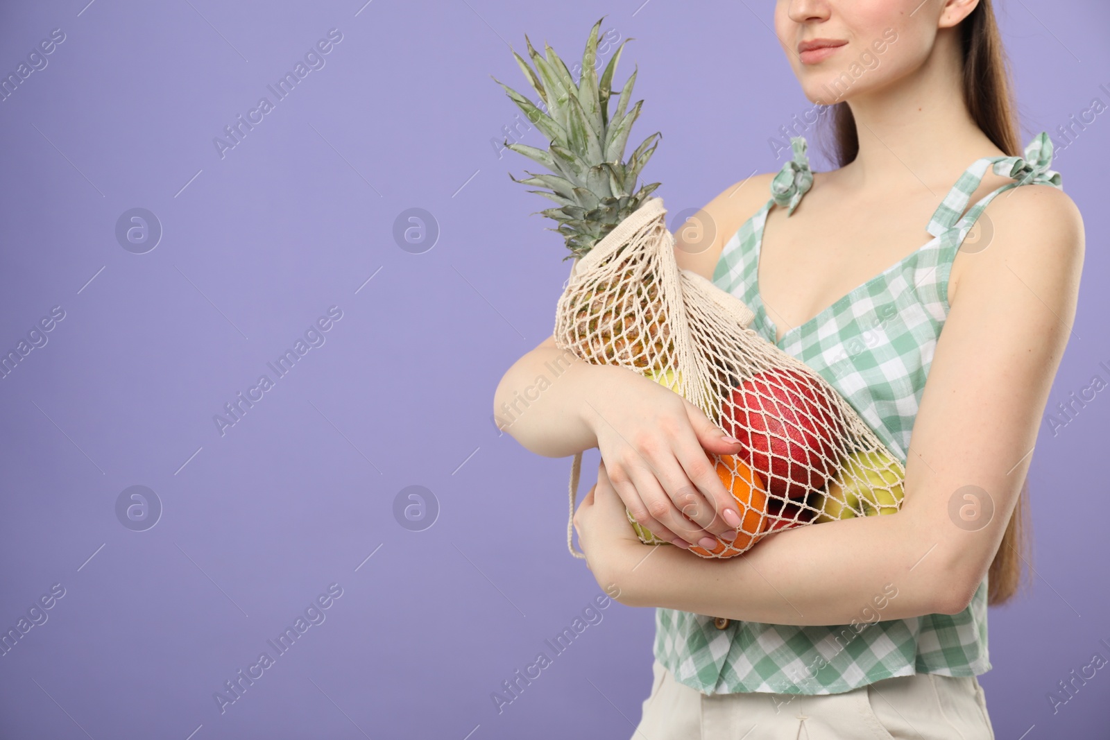 Photo of Woman with string bag of fresh fruits on violet background, closeup. Space for text