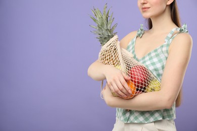 Photo of Woman with string bag of fresh fruits on violet background, closeup. Space for text