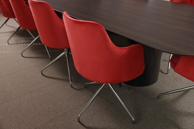 Photo of Stylish red office chairs and large wooden table in empty conference room