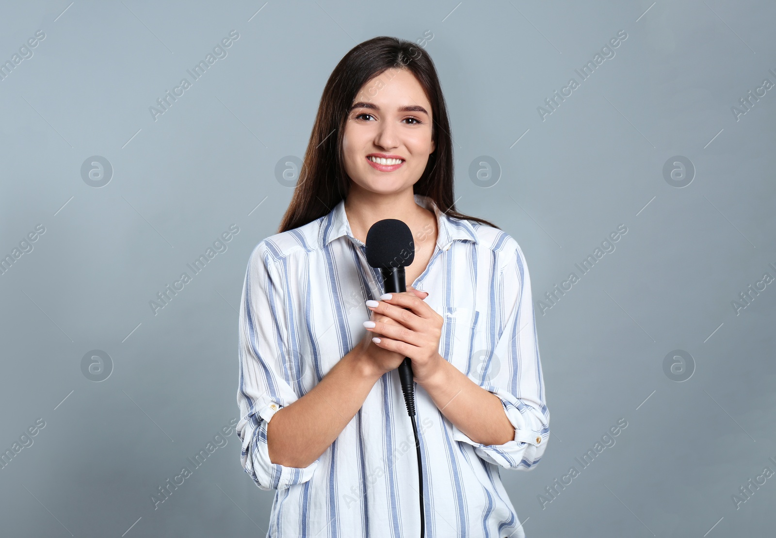 Photo of Young female journalist with microphone on grey background