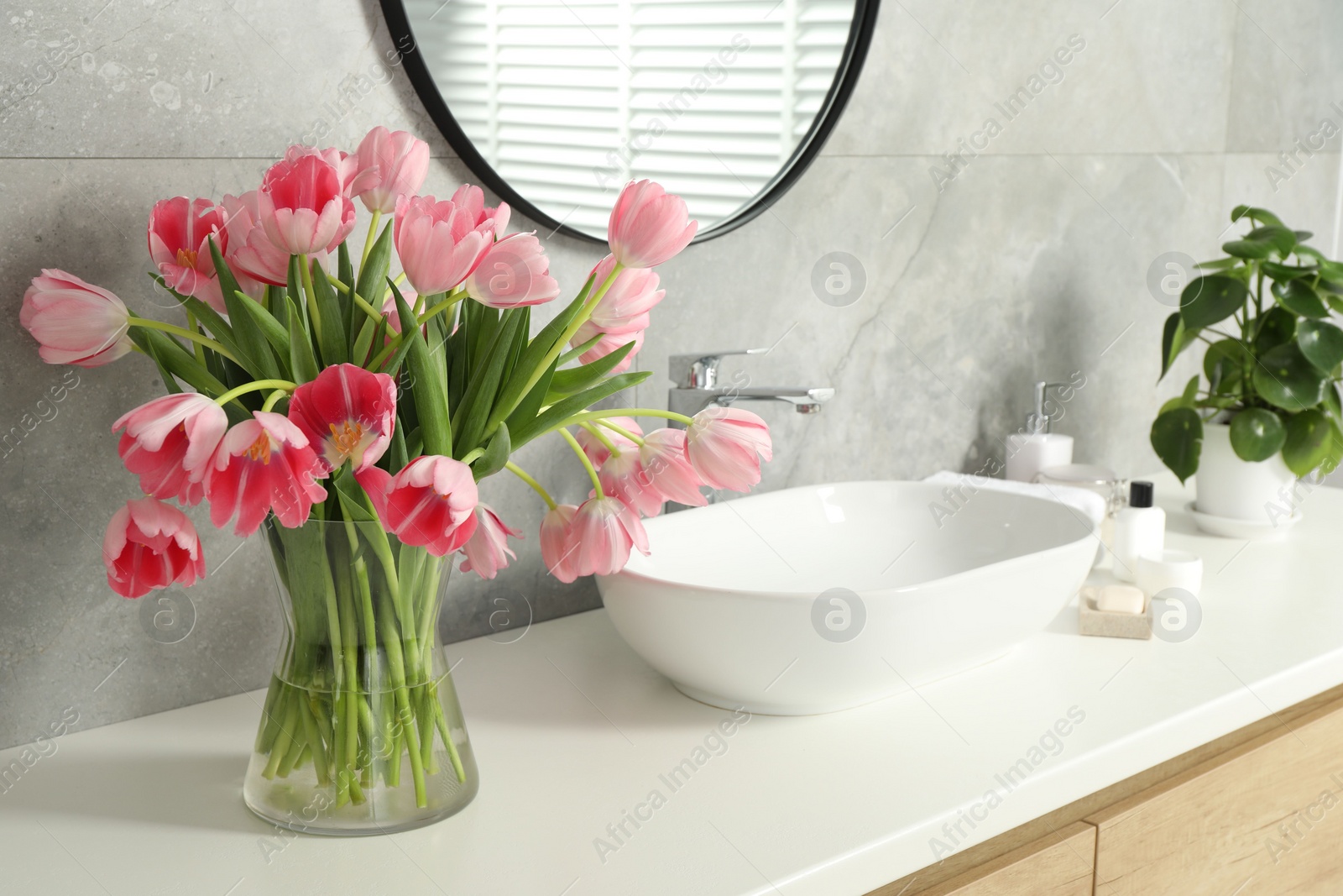 Photo of Vase with beautiful pink tulips and toiletries near sink in bathroom