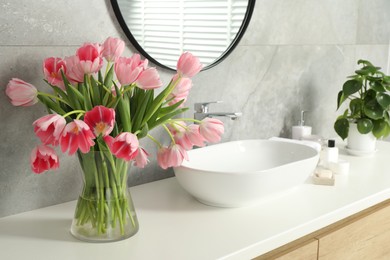 Photo of Vase with beautiful pink tulips and toiletries near sink in bathroom