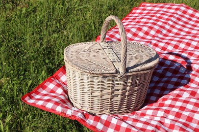 Photo of Picnic basket with checkered tablecloth on green grass outdoors
