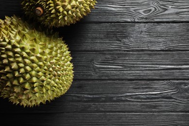 Photo of Ripe durians on black wooden table, flat lay. Space for text