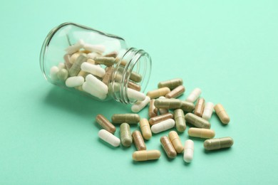 Photo of Vitamin pills and bottle on mint color background, closeup