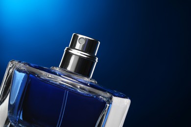 Photo of Luxury men`s perfume in bottle against dark blue background, closeup. Space for text