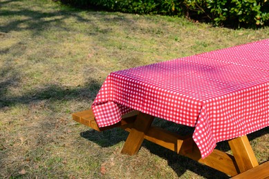 Photo of Empty picnic table with red and white checkered tablecloth in park on sunny day