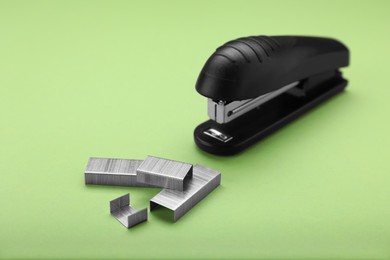 Photo of New bright stapler with staples on green background. School stationery