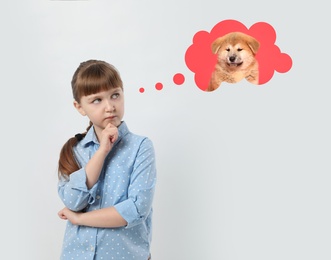 Image of Little girl on light background dreaming about cute puppy