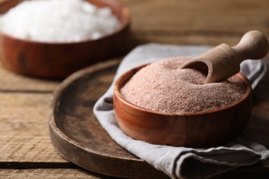 Photo of Different salt and scoop in bowl on wooden table, closeup. Space for text