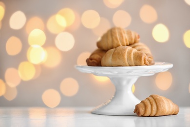 Cake stand with tasty pastry on table against blurred lights, space for text