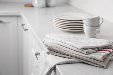 Photo of Stack of soft kitchen towels and dishware on countertop indoors, space for text