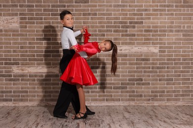 Photo of Beautifully dressed couple of kids dancing together near brick wall indoors