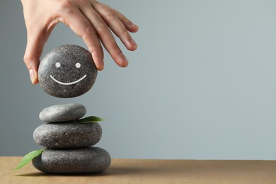 Photo of Woman putting stone drawn happy face onto stack against grey background, closeup and space for text. Zen concept