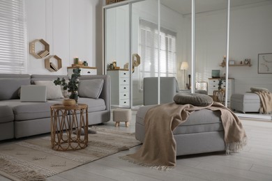 Photo of Comfortable grey sofa, ottoman and wardrobe with mirror doors in living room interior