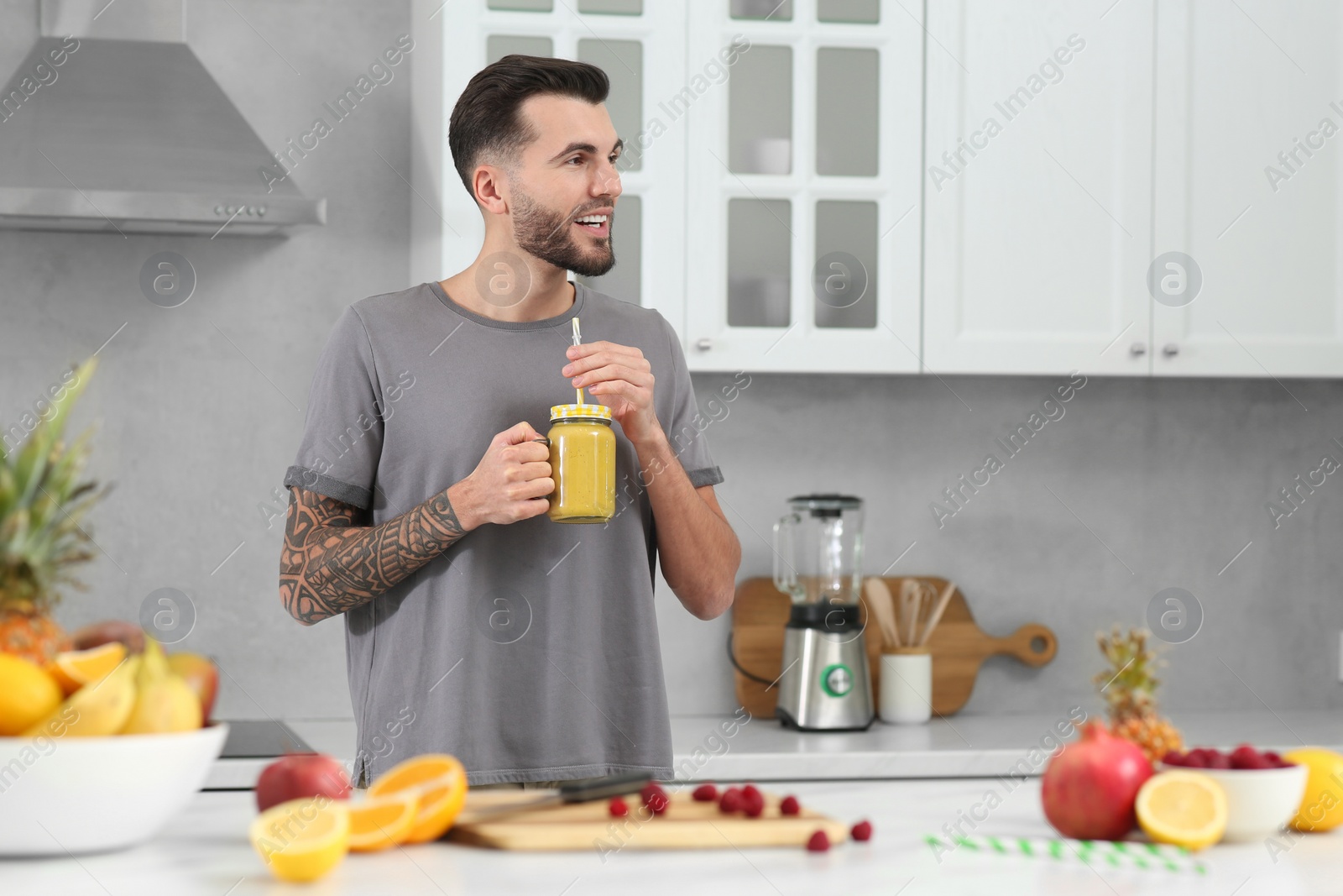 Photo of Handsome man with delicious smoothie in kitchen. Space for text