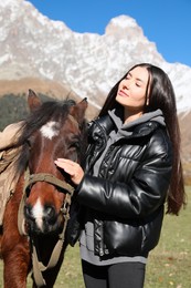 Photo of Young woman stroking horse in mountains on sunny day. Beautiful pet
