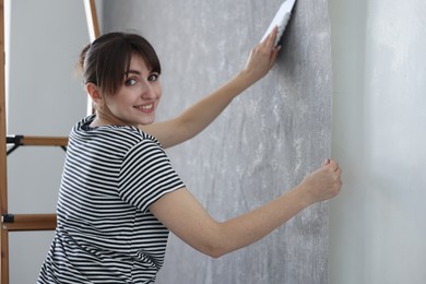 Photo of Woman smoothing stylish gray wallpaper in room