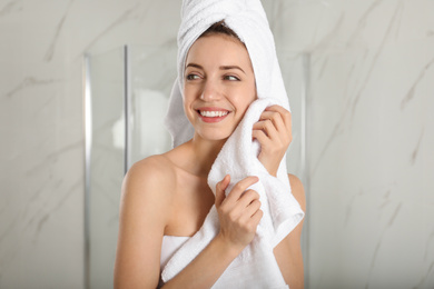 Photo of Young woman wiping face with towel in bathroom