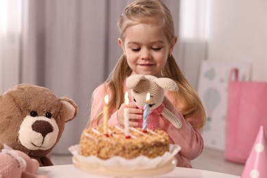 Photo of Cute girl with birthday cake and toys at table indoors