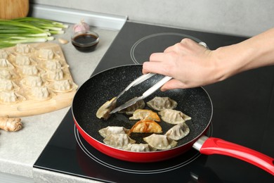 Photo of Woman cooking gyoza on frying pan with hot oil in kitchen, closeup