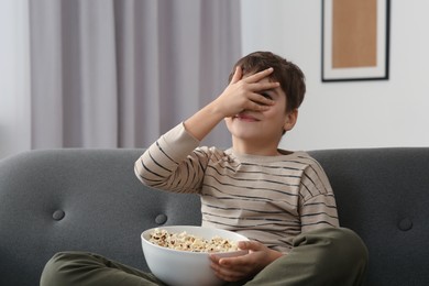 Photo of Little boy with popcorn covering face near TV at home