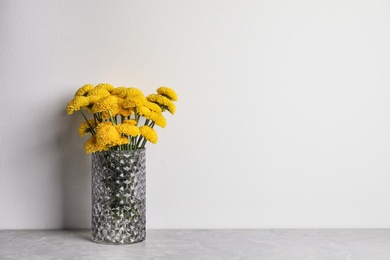 Photo of Bouquet of beautiful yellow flowers in glass vase on grey table against white background. Space for text