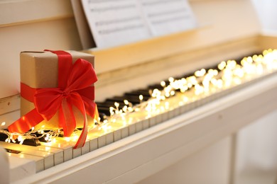 Photo of Gift box and fairy lights on piano keys, space for text. Christmas music