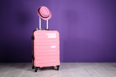 Travel suitcase with hat and sunglasses on wooden floor near purple wall, space for text. Summer vacation