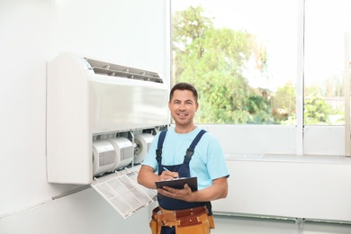 Photo of Technician with clipboard near air conditioner indoors